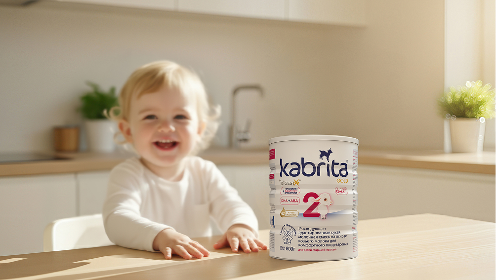 Улыбающийся малыш сидит рядом с банкой Kabrita
